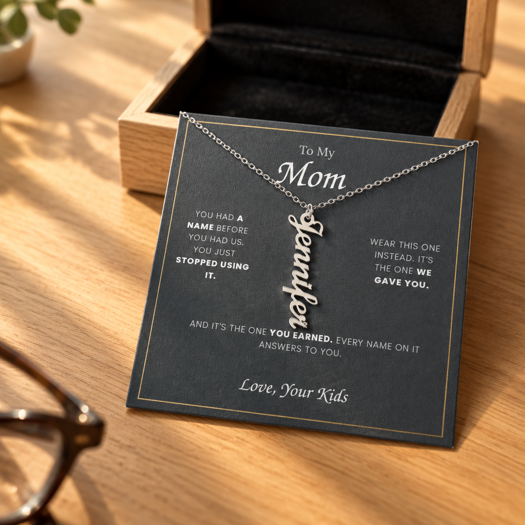 Name necklace and its message card on an oak table in warm morning light, reading glasses nearby