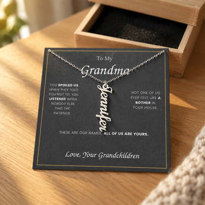 Name necklace and its message card on an oak table beside the open wooden gift box